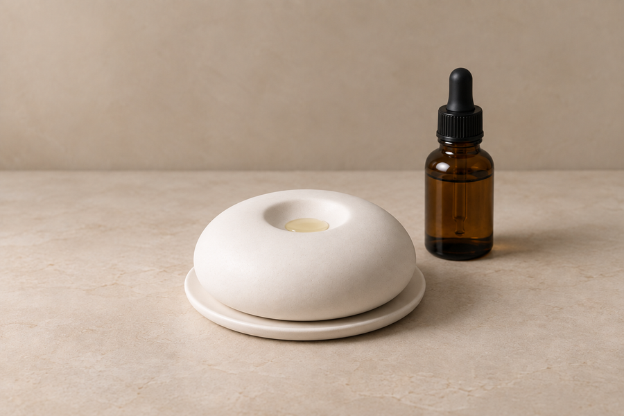 White aroma stone diffuser and saucer beside an amber dropper bottle