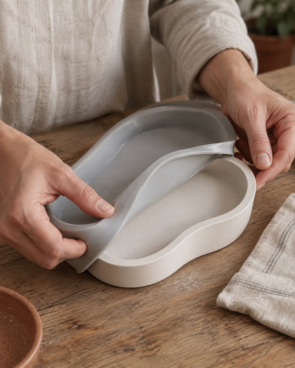 Hands peeling a silicone mould away from a pale cast dish